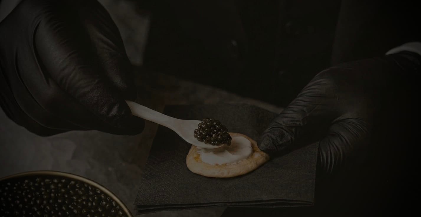 Close-up of a gloved hand serving caviar on a blini with a spoon